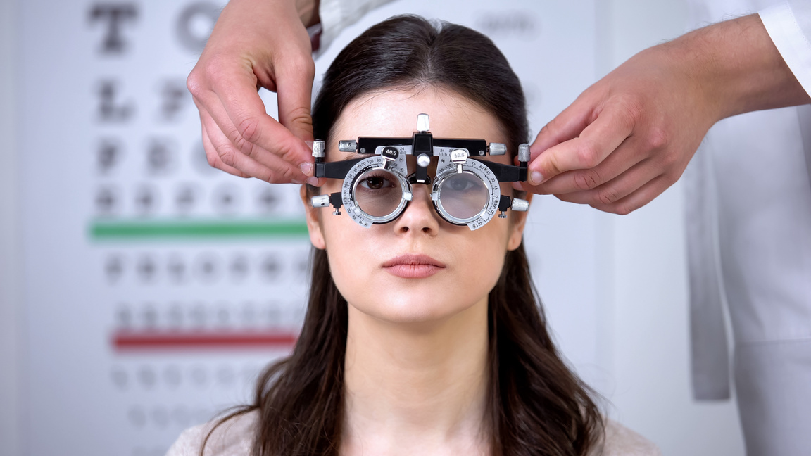 Oculist putting optical trial frame on girl sight correction diopter measurement